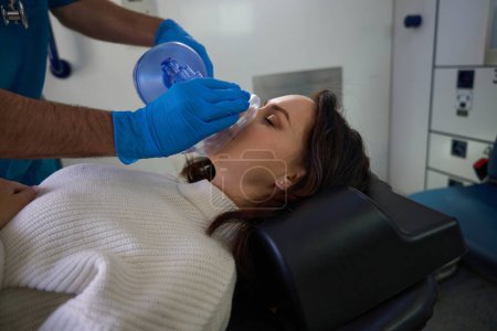 Foto de Mujer inconsciente se encuentra en el interior de un vehículo de cuidados intensivos, mientras que un trabajador médico proporciona oxígeno - Imagen libre de derechos