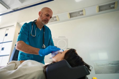 Foto de Mujer desmayada yace en la ambulancia con los ojos cerrados mientras un trabajador médico proporciona oxígeno - Imagen libre de derechos