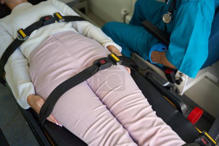 Téléchargez les photos : La patiente s'allonge sur le dos avec les bras tendus le long du corps et fixés avec des bretelles pendant qu'un urgentiste s'assoit à côté d'elle - en image libre de droit