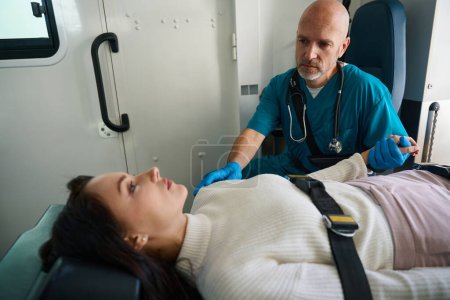 Téléchargez les photos : La patiente s'allonge sur le dos, attachée par les ceintures de sécurité dans une ambulance, tandis qu'un médecin ambulancier s'assoit à côté d'elle - en image libre de droit