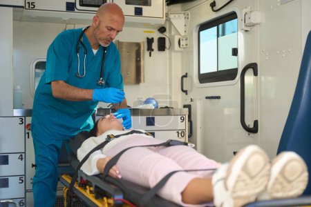 Foto de Hombre ansioso se para sobre la cara de la paciente mientras ella se acuesta en una camilla en una ambulancia - Imagen libre de derechos