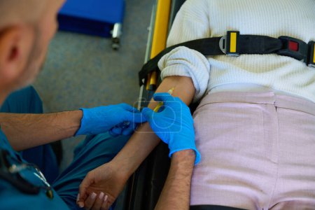 Foto de Médico profesional inyecta a una paciente mientras se acuesta en una camilla inmovilizada por un cinturón - Imagen libre de derechos