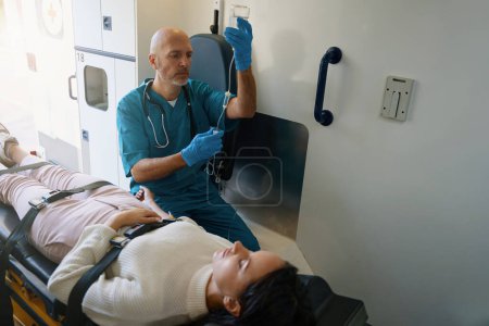 Photo for Concentrated doctor preparing to inject a patient while she lies unconscious on a gurney - Royalty Free Image