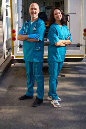 Photo for Confident man and woman are standing on the street in medical uniforms while a company vehicle is parked behind them - Royalty Free Image