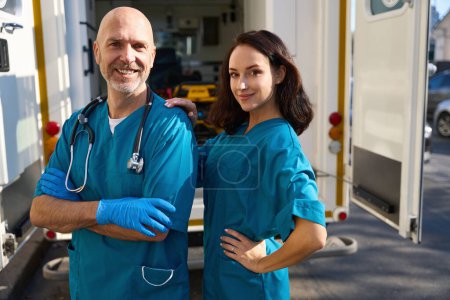 Photo for Encouraged woman dressed in medical gear stands near man while he smiles with arms crossed over chest - Royalty Free Image