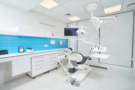 Spacious dentist office with empty leather dental chair and bright overhead lighting