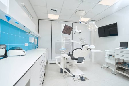 Photo for Roomy modern well-lit professional dentist office with empty leather chair for patient - Royalty Free Image