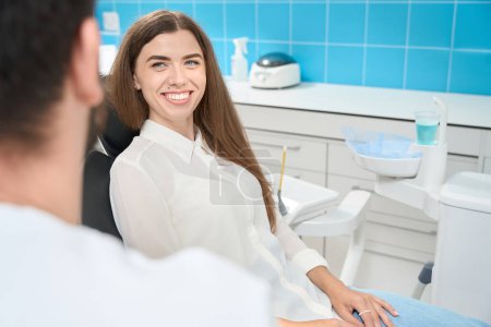 Foto de Sonriendo satisfecho joven cliente clínica dental comunicarse con el dentista durante la consulta primaria - Imagen libre de derechos