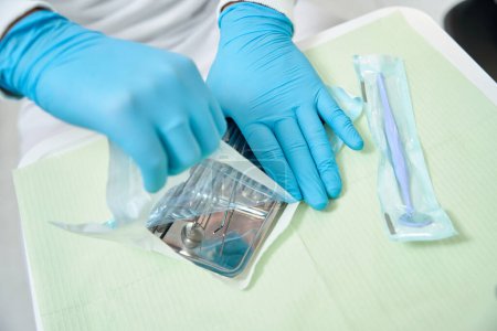 Foto recortada de manos estomatólogas en guantes de nitrilo abriendo bolsa de esterilización autosellante con herramientas dentales esterilizadas