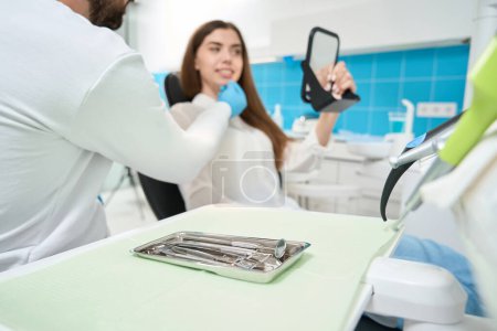 Foto de Paciente mirando sus dientes en el espejo de la mano mientras escucha al estomatólogo durante la cita - Imagen libre de derechos