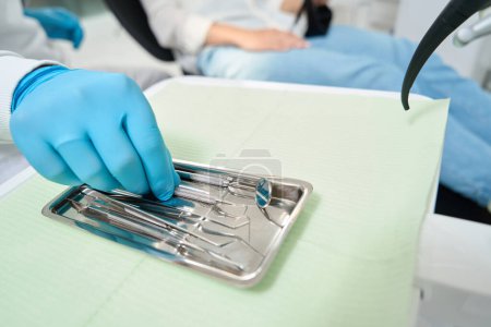 Photo for Cropped photo of doctor hand in nitrile glove reaching for dental probe on instrument tray - Royalty Free Image