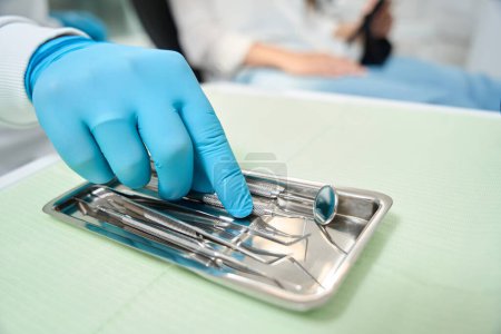 Photo for Close-up of stomatologist hand in nitrile glove taking dental explorer from instrument tray - Royalty Free Image