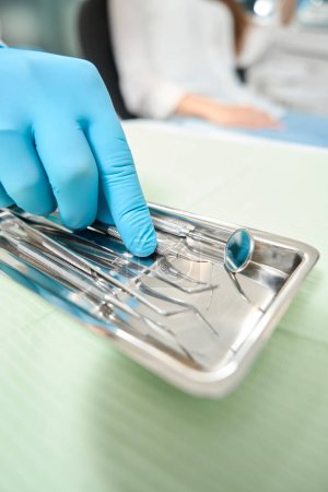 Foto de Foto recortada de la mano del dentista en guante de nitrilo tomando sonda dental de la bandeja de instrumentos - Imagen libre de derechos
