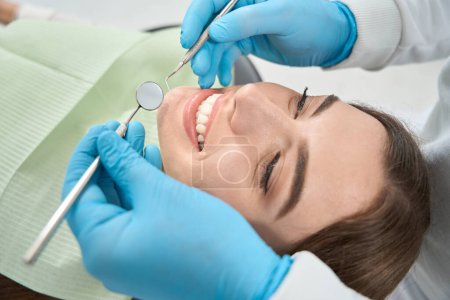 Photo for Dentist in nitrile gloves holding mouth mirror and dental probe over smiling patient face - Royalty Free Image