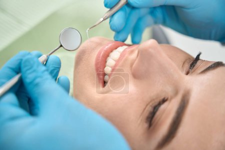 Photo for Close-up of dentist hands in nitrile gloves holding dental explorer and mouth mirror over smiling woman face - Royalty Free Image