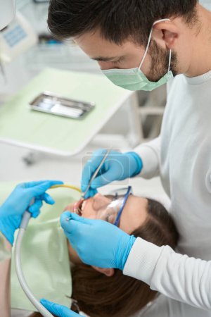 Téléchargez les photos : Stomatologue regardant les dents du jeune patient à l'aide d'un miroir buccal et d'une sonde dentaire - en image libre de droit