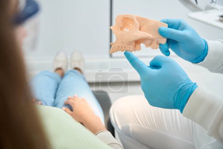 Ausgeschnittenes Foto eines Stomatologen, der auf poröse vordere Zähne am Oberkiefermodell zeigt