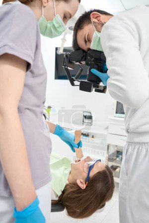 Photo for Dentist taking photos of patient teeth assisted by nurse using tongue depressor - Royalty Free Image