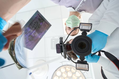 Foto de Bajo ángulo del estomatólogo tomando fotos dentales del paciente asistido por la enfermera - Imagen libre de derechos
