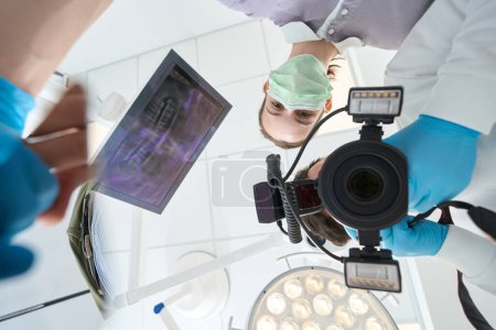 Téléchargez les photos : Angle bas du dentiste prenant des images au début de l'examen du patient assisté par une infirmière - en image libre de droit