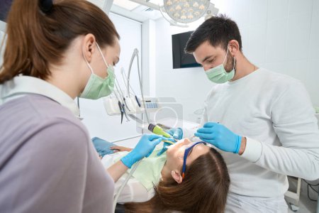 Foto de Estomatólogo extirpando tejido carioso en diente paciente con taladro dental asistido por enfermera - Imagen libre de derechos
