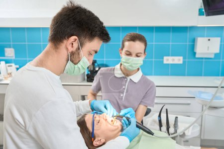 Foto de Dentista enfocado en guantes de nitrilo usando escamador dental piezoultrasónico en esmalte dental femenino - Imagen libre de derechos