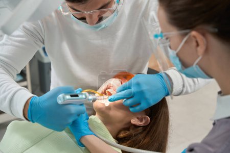 Téléchargez les photos : Stomatologue injectant un anesthésique local dans la gencive d'une patiente avec une seringue dentaire assistée par une infirmière - en image libre de droit