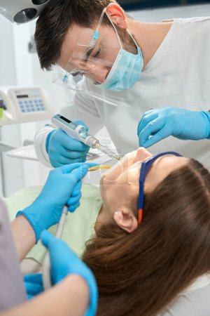 Foto de Estomatólogo serio enfocado que administra anestesia a una paciente femenina mientras la enfermera sostiene el eyector de saliva - Imagen libre de derechos