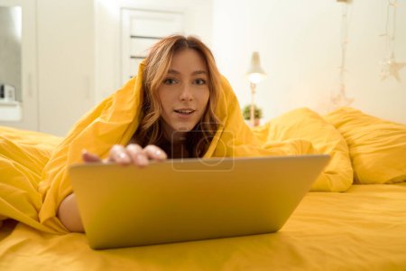 Téléchargez les photos : Tranquil concentrated female lying in bed wrapped in duvet with portable computer - en image libre de droit