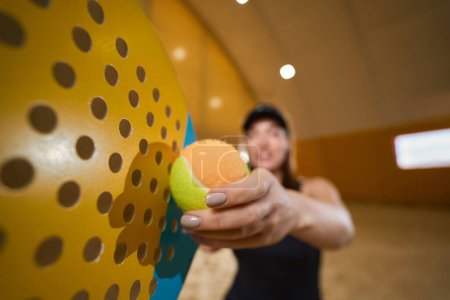 Téléchargez les photos : Athletic female holds a tennis ball in her hands next to a racket while she is in an indoor playing area - en image libre de droit