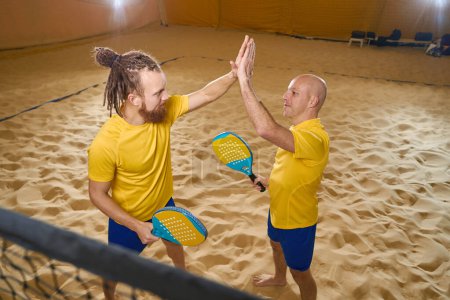 Téléchargez les photos : Confident men in yellow t-shirts touch with palms of one hand while holding racket - en image libre de droit