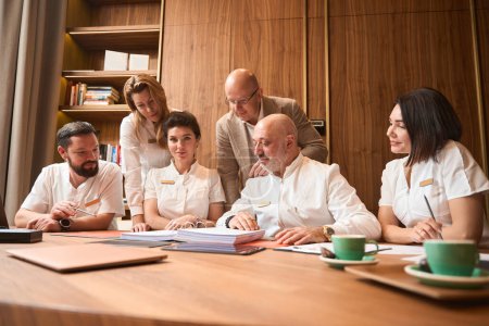 Téléchargez les photos : Team of doctors is seated in a large office at a table, discussing a treatment plan - en image libre de droit