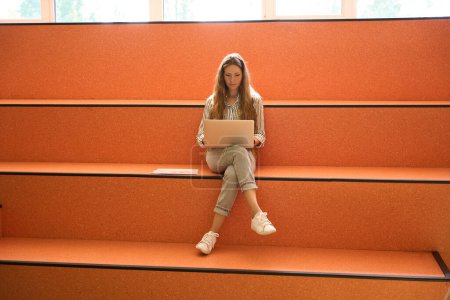 Téléchargez les photos : Young pretty lady working with laptop while sitting on steps, copy space - en image libre de droit