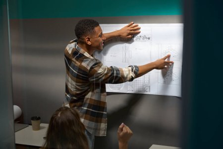 Foto de African American man using drawing while showing it for his female colleague in the office - Imagen libre de derechos