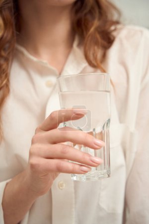 Téléchargez les photos : Cropped photo of well-groomed female hand holding glass filled with transparent liquid - en image libre de droit