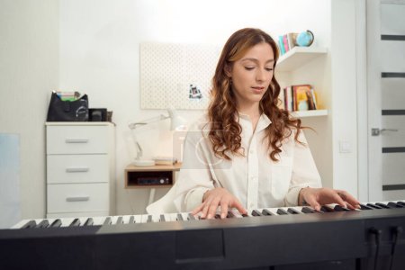 Foto de Waist-up portrait of serious young female musician performing musical composition on synthesizer - Imagen libre de derechos
