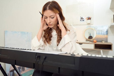 Téléchargez les photos : Waist-up portrait of focused female composer sitting at synthesizer and reading sheet music - en image libre de droit