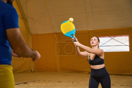 Foto de Tense female in a sports uniform is practicing a shot in enclosed space while a man is watching in front - Imagen libre de derechos