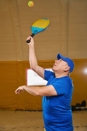 Photo for Serious tennis player in sportswear is going to hit the tennis ball with a racket while standing in the sports hall - Royalty Free Image