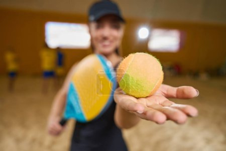 Foto de Satisfied female in a sports uniform stands on a sandy field indoors while sports equipment is in hands - Imagen libre de derechos