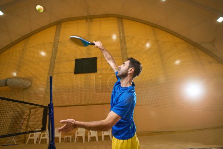 Photo for Focused frescoball player in sportswear is on the sand court indoors while addicted to the game - Royalty Free Image