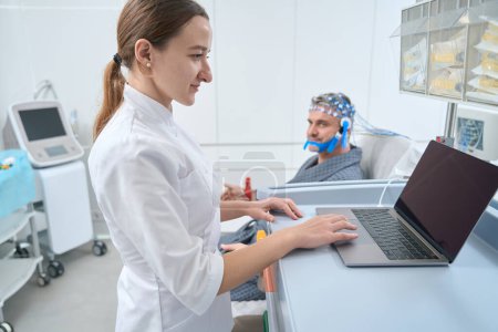 Foto de Woman diagnostician at the workplace conducts EEG - electroencephalography, the patient is located in a special chair - Imagen libre de derechos