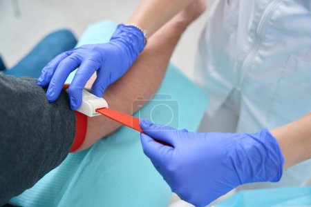Téléchargez les photos : Nurse carefully tightens the tourniquet on the man arm, this is preparation for blood sampling - en image libre de droit