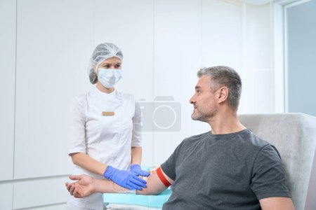 Téléchargez les photos : Man takes a blood test from a vein, a nurse carefully performs the procedure - en image libre de droit