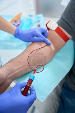 Téléchargez les photos : Nurse takes a blood sample from a vein from a patient in a medical clinic, she works in protective gloves - en image libre de droit