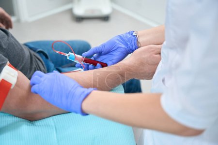 Téléchargez les photos : Nurse takes a blood sample from a patient in a medical clinic, she works in protective gloves - en image libre de droit