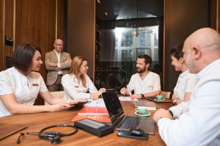 Téléchargez les photos : Head of the medical clinic communicates with colleagues in a business friendly atmosphere, the team is seated at large table - en image libre de droit