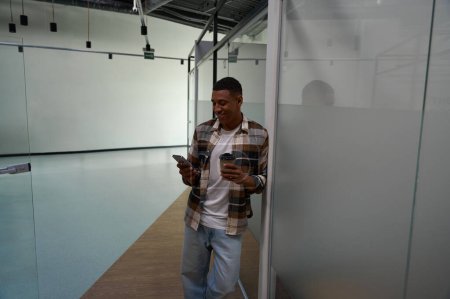 Téléchargez les photos : Happy African American man holding smartphone and coffee in the office - en image libre de droit