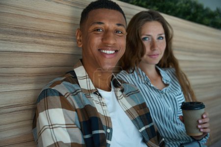 Téléchargez les photos : Smiling African American man sitting next to his female colleague in the office - en image libre de droit