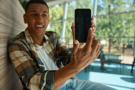 Téléchargez les photos : Smiling African American man pointing his finger at phone screen - en image libre de droit